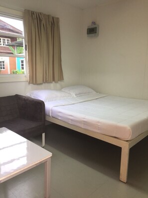 Habitación individual con una cama blanca, una mesita, una silla y un ventanal con cortinas.