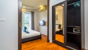 A modern hotel room with a wooden floor, a bed, a TV, and a wardrobe with a control panel. - Heaven Lagoon Apartments by Lofty (Patong)