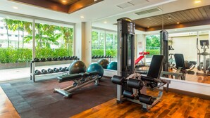 A gym with exercise equipment, large windows, and a view of greenery outside. - Heaven Lagoon Apartments by Lofty (Patong)