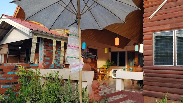 Un edificio rústico de madera con fachada de ladrillo, un paraguas grande y diversas plantas y adornos.