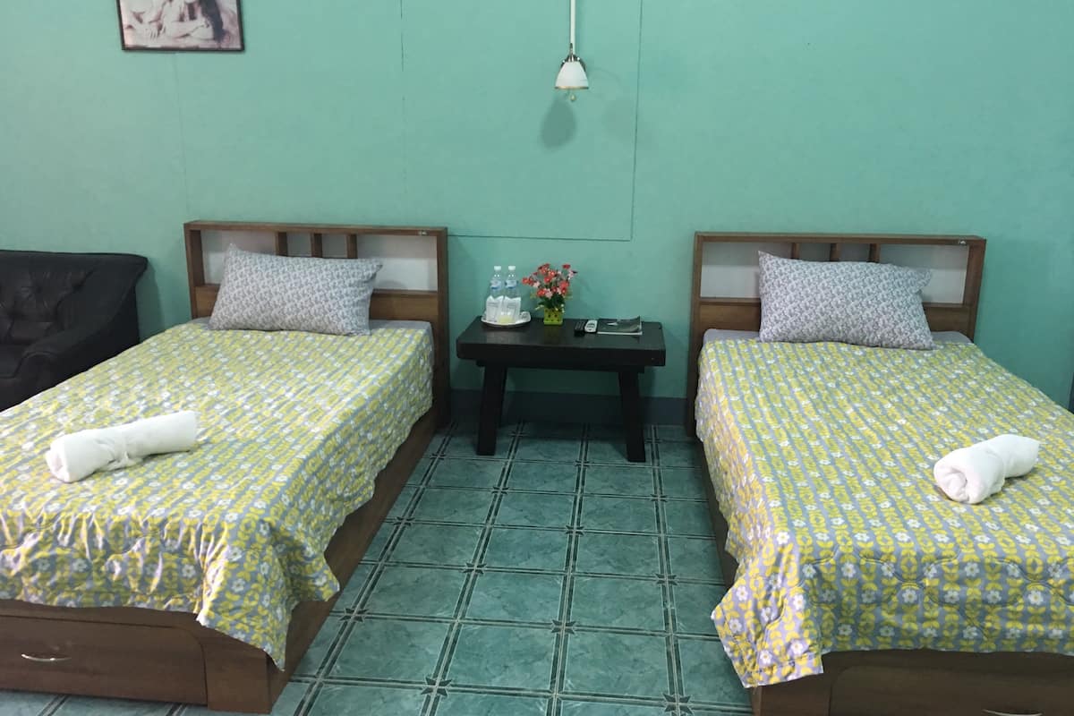 A twin room with two beds, each with a patterned bedspread and pillows, a small table with a vase of flowers, and a picture on the wall.