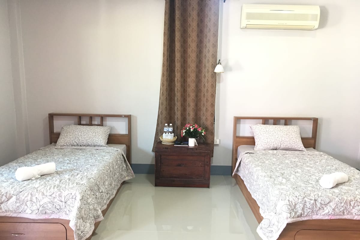 A room with two beds, a nightstand, a lamp, and an air conditioner.