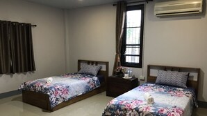 Habitación de hotel con dos camas, cada una con cubrecama floral, una mesita de noche con lámpara y un equipo de aire acondicionado en la pared.