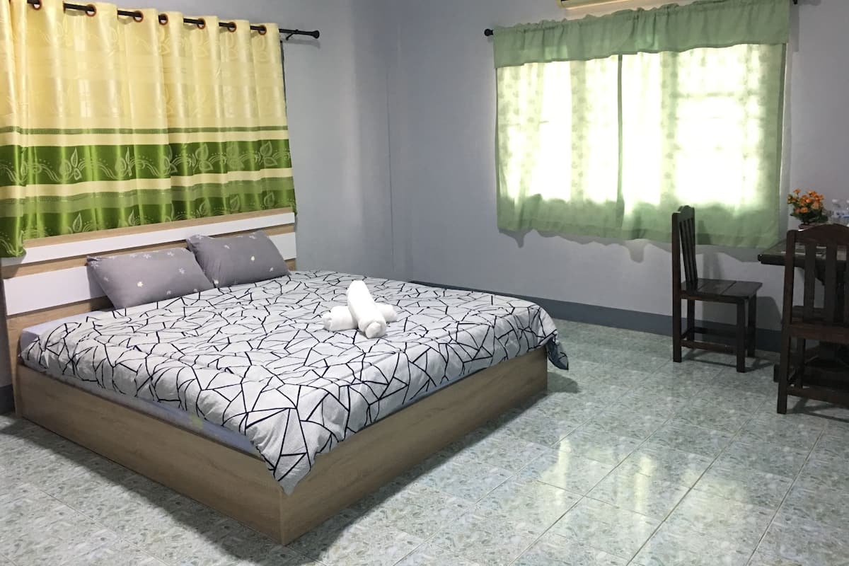 A bedroom with a bed, a chair, a table, and a window with curtains.