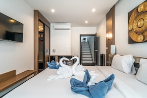 A hotel room with a bed, a TV, a staircase, and a wall-mounted artwork.