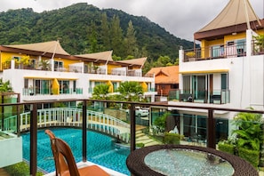 A hotel with a swimming pool, multiple balconies, and a view of a forested mountain.