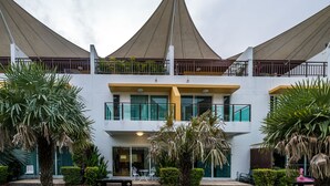 A modern hotel with a central atrium, multiple balconies, and a covered outdoor area with palm trees. - AP Grand Residence by Lofty (Kamala)