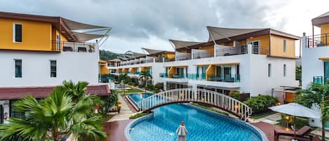 A hotel with a pool, multiple balconies, and a tropical garden.