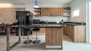 A modern kitchen with wooden cabinets, a black countertop, and a central island with bar stools. - AP Grand Residence by Lofty (Kamala)