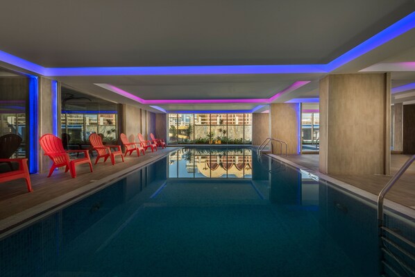 Una piscina con sillas rojas y vistas a edificios a través de las ventanas.