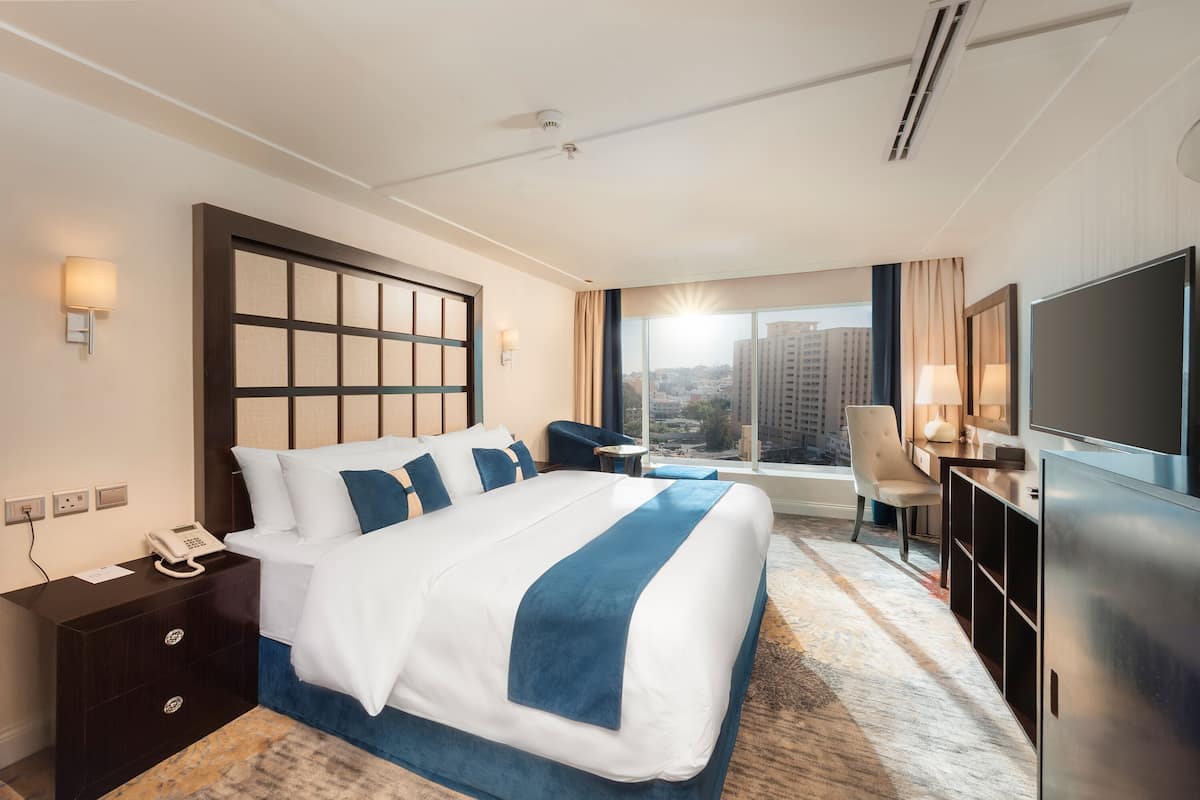 A hotel room with a large bed, a desk, a TV, and a view of the city.
