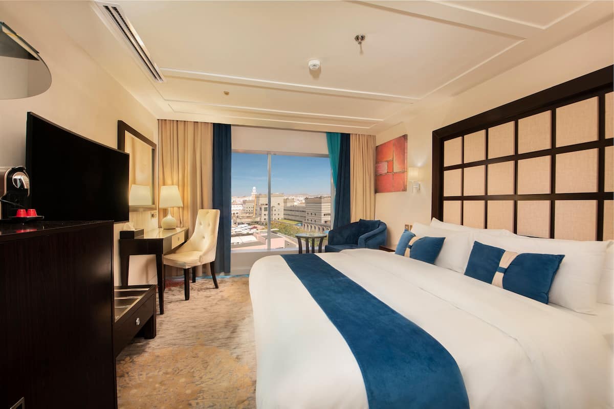 A hotel room with a large bed, a desk, a chair, a television, and a view of the city.