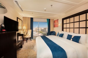 A hotel room with a large bed, a desk, a chair, a television, and a view of the city.