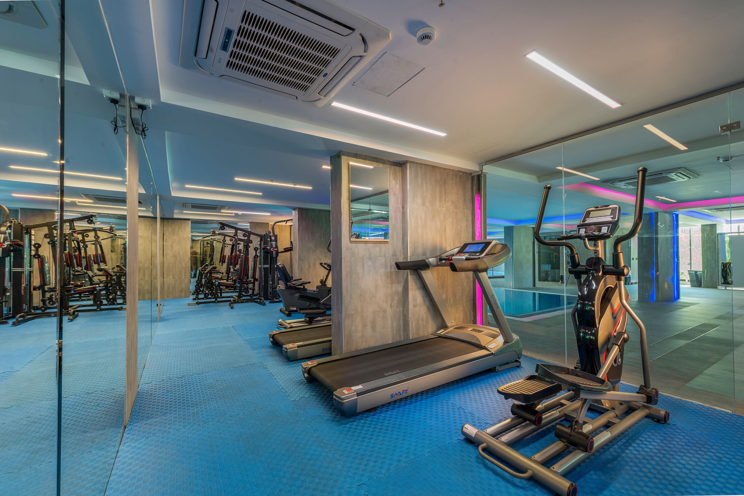 A modern gym with treadmills, elliptical machines, and weight equipment.