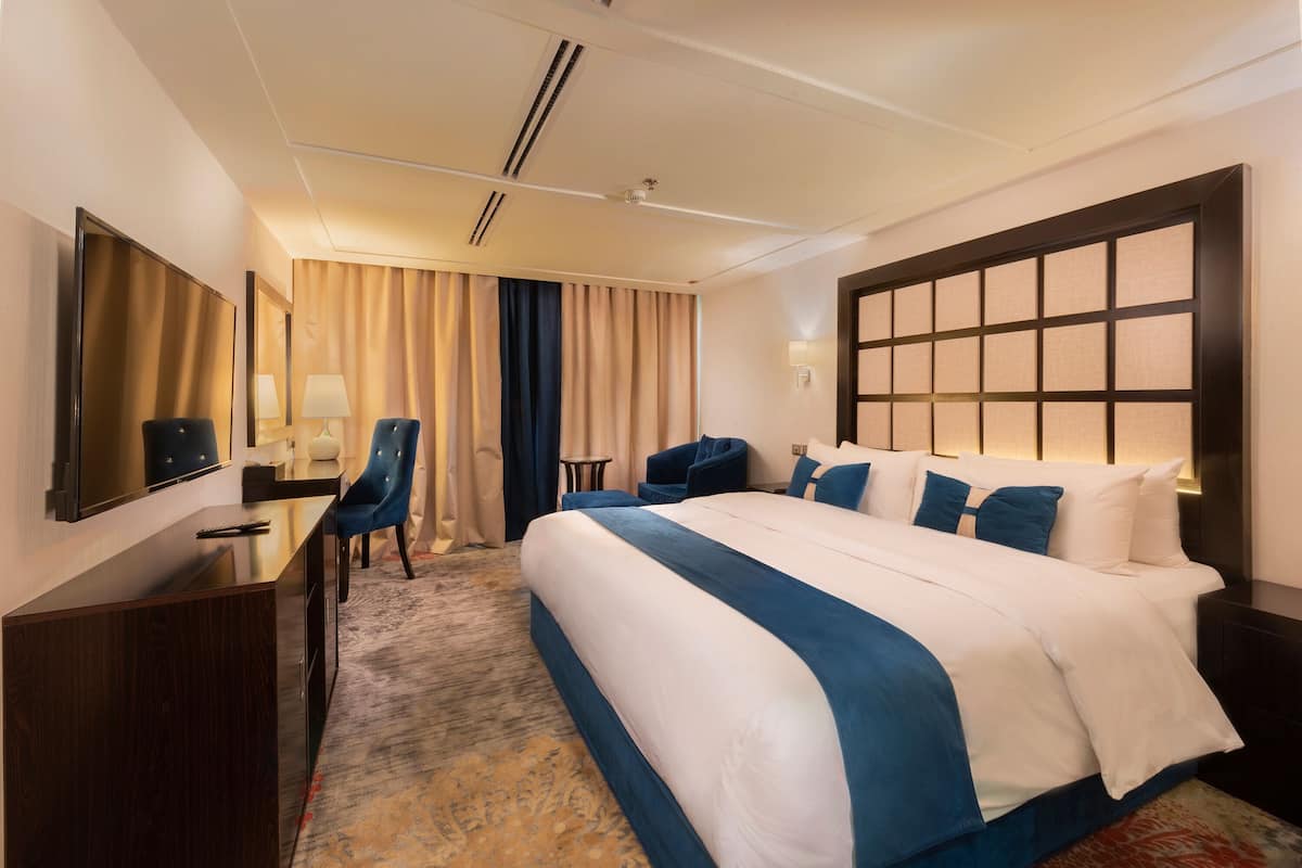 A hotel room with a large bed, a desk, a chair, a TV, and a window with curtains.