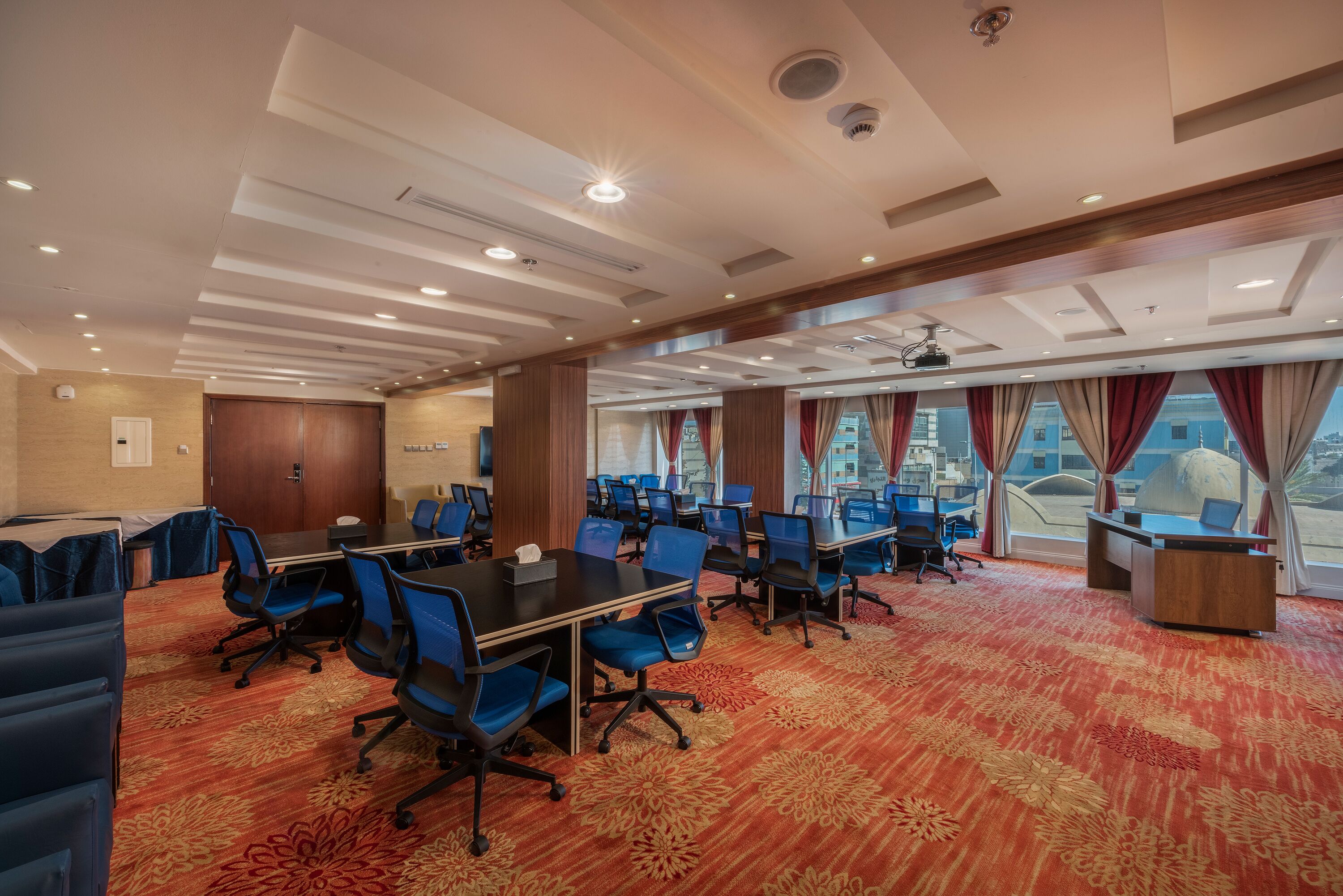 A conference room with multiple tables, blue chairs, and a red carpet.