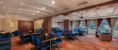 A conference room with multiple tables, blue chairs, and a red carpet.