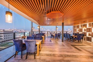 A rooftop terrace with wooden slatted ceiling, tables, chairs, and hanging pendant lights. - Blue Inn (Abha)
