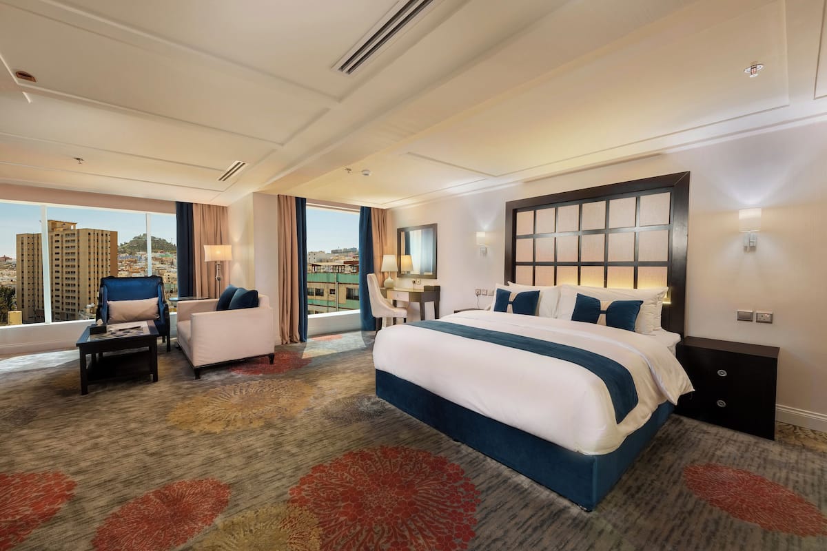 A hotel room with a large bed, a sofa, a desk, and a view of the city.