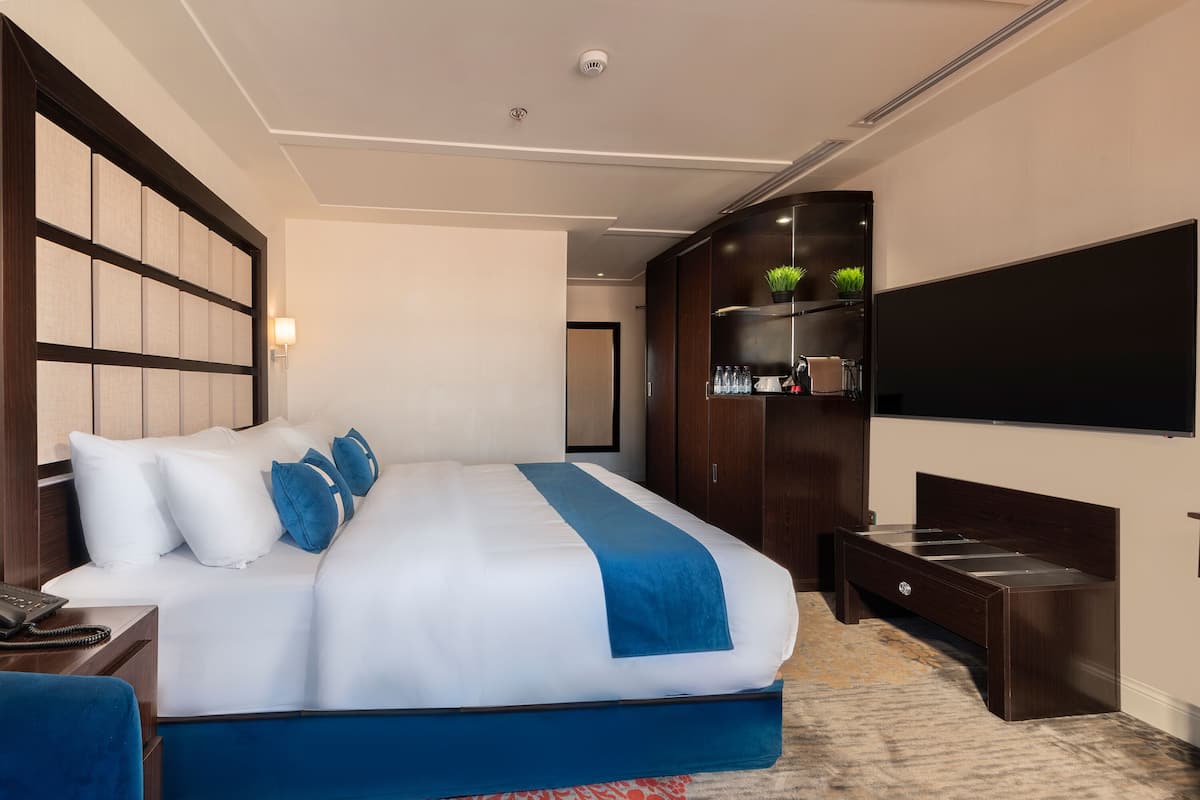 A modern hotel room with a large bed, a flat-screen TV, a wardrobe, and a desk with a telephone.