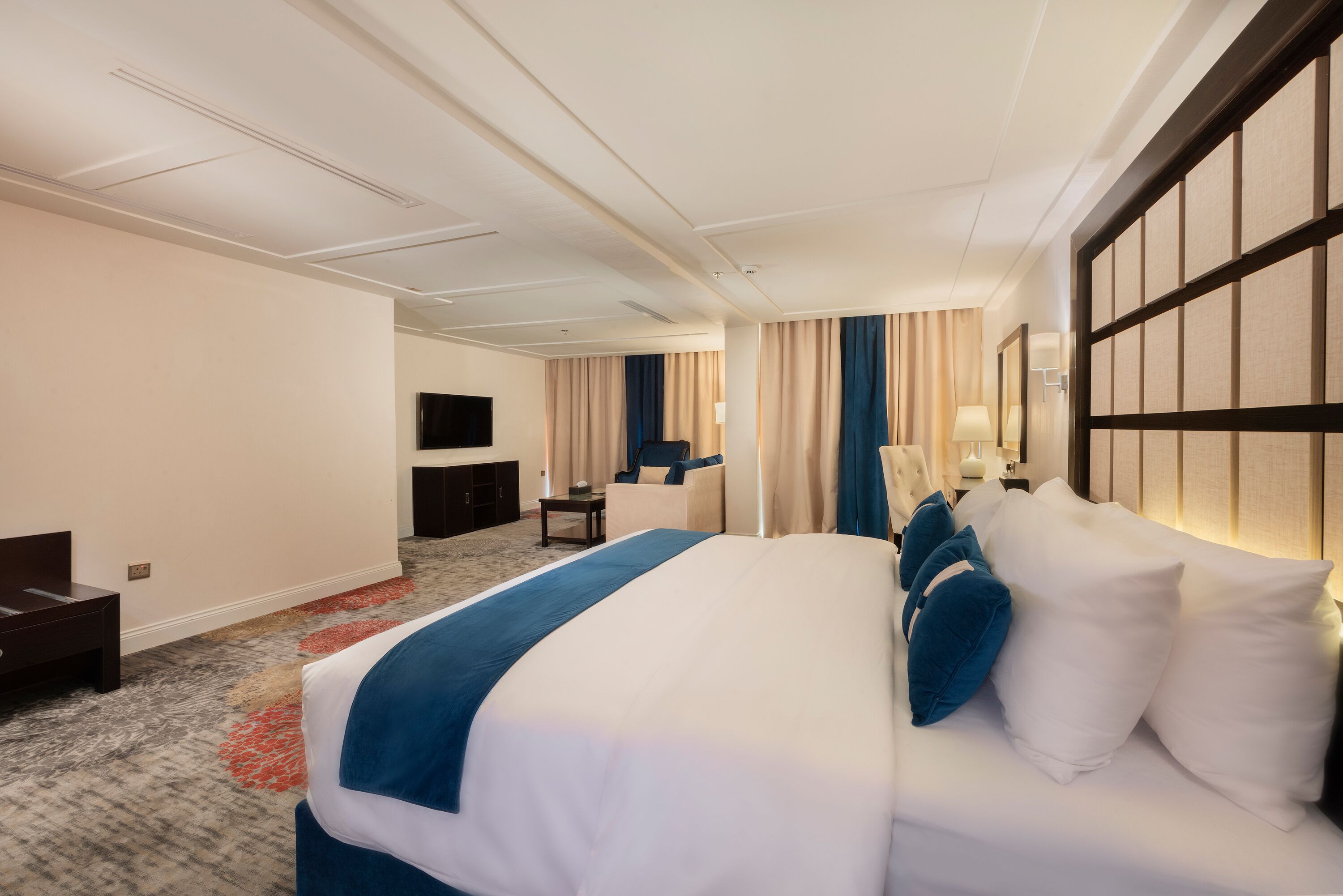 A hotel room with a large bed, a desk, a chair, and a TV.
