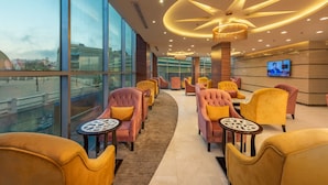 A modern lounge area with plush seating, a large TV screen, and a view of the cityscape through large windows. - Blue Inn (Abha)