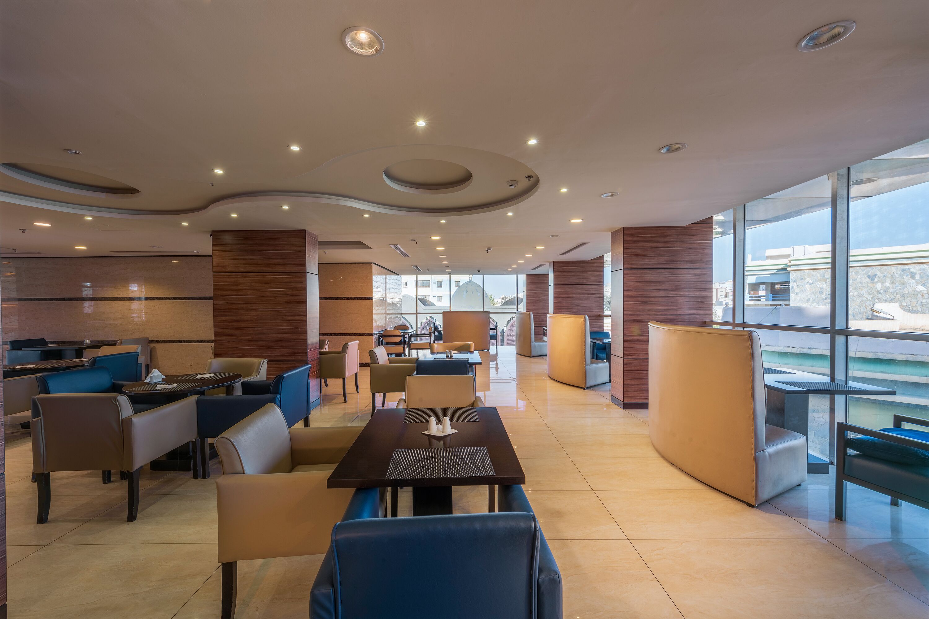 A modern hotel lobby with a central seating area, a bar, and large windows offering a view.