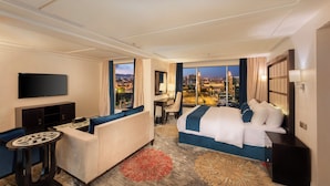 A hotel room with a large bed, a sofa, a desk, and a TV. The room has a city view. - Blue Inn (Abha)