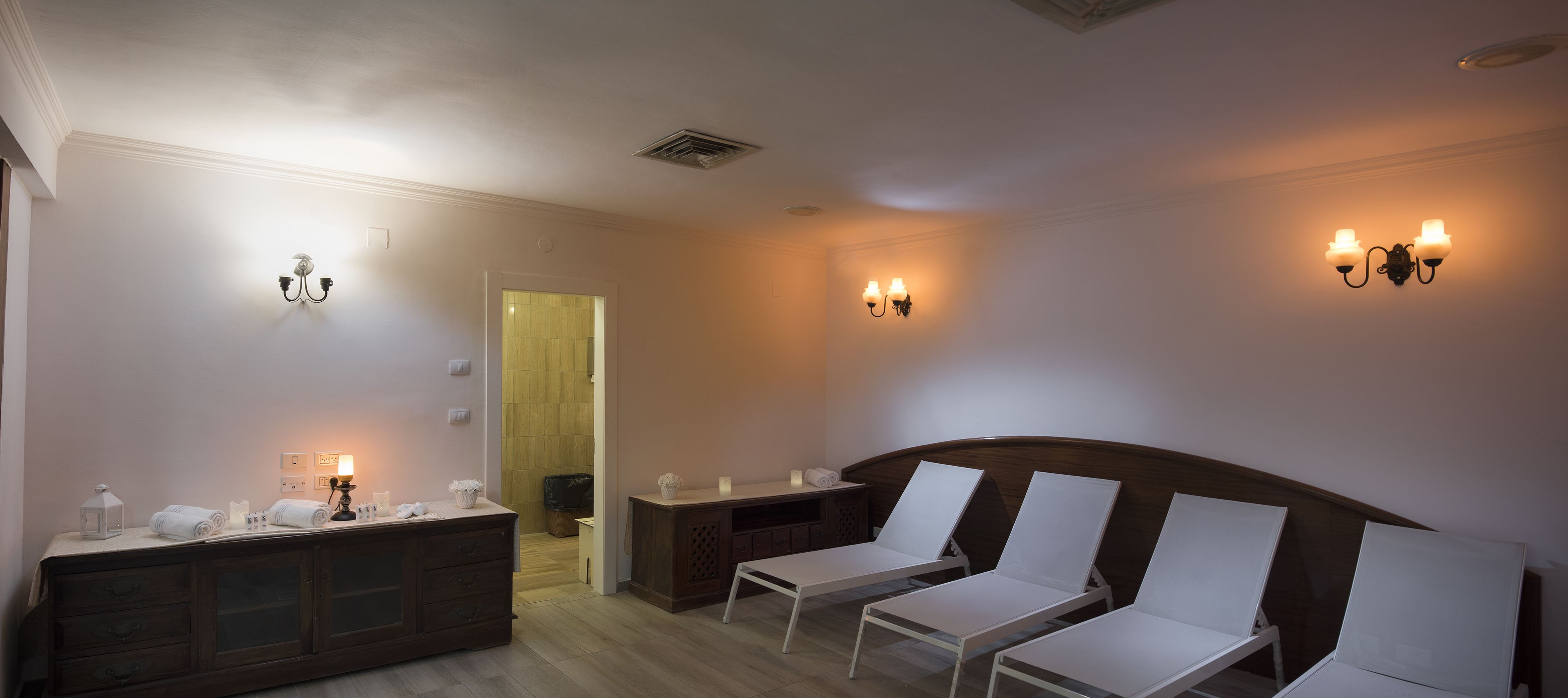 Une pièce comprenant un lit, deux chaises blanches, une coiffeuse avec un miroir et des appliques murales.