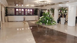 A spacious lobby with a reception desk, a glass-top table with a floral arrangement, and a polished tile floor.