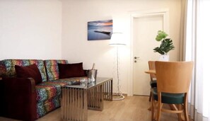 A living room with a colorful sofa, a small table, a floor lamp, and a wooden chair. - Kinorot Hotel - kosher Le'mehadrin (Tiberias)