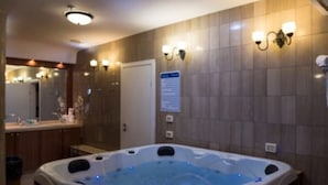 A bathroom with a hot tub, a mirror, a sink, and wall sconces.