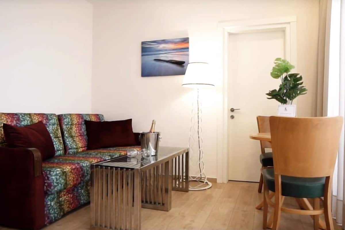 A living area with a sofa, a coffee table, a floor lamp, and a dining table with chairs.