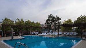A rectangular swimming pool with a tiled deck, surrounded by lounge chairs and a pergola structure.