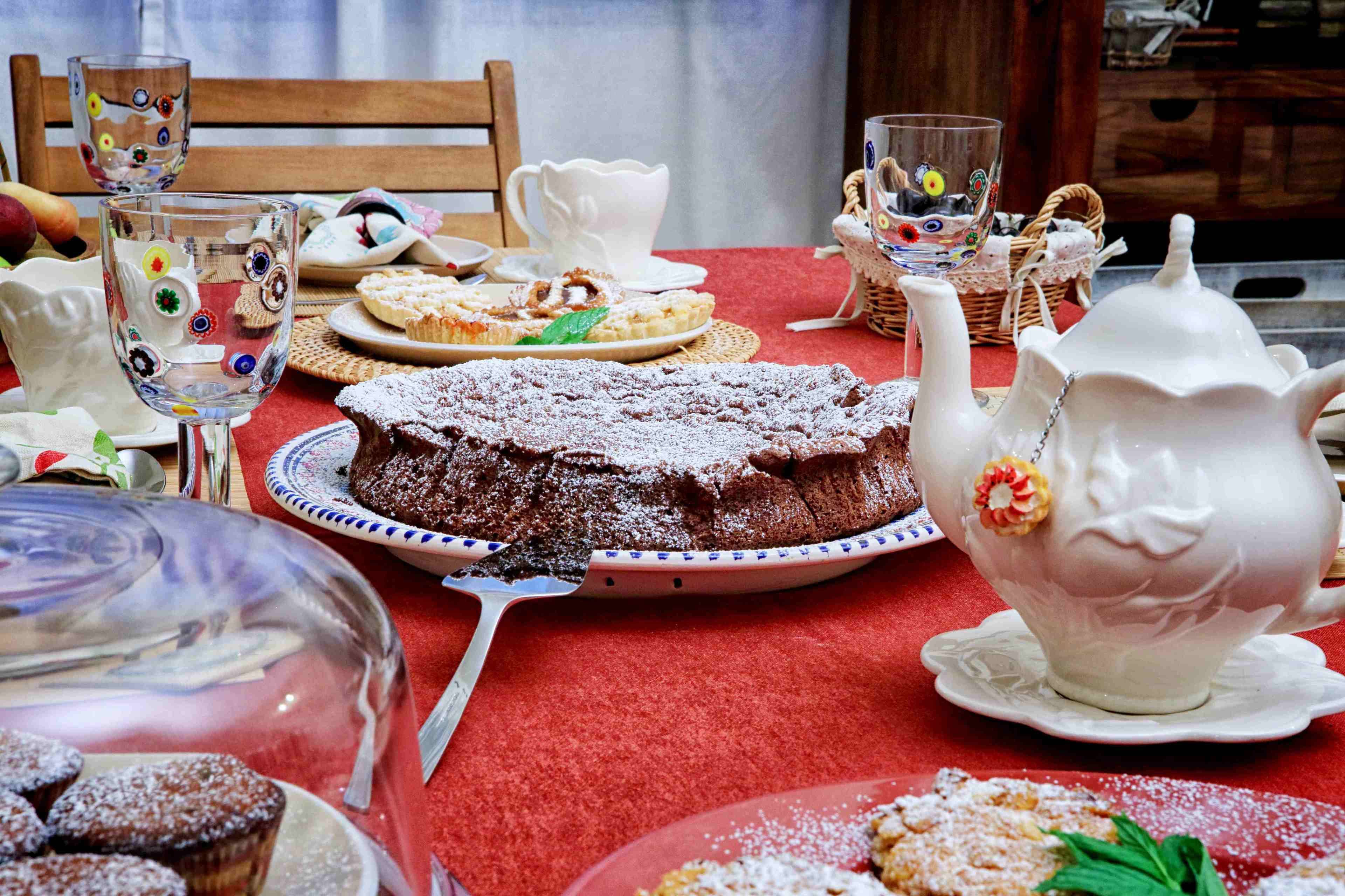A table set with various desserts, including a chocolate cake, and white teacups and saucers.