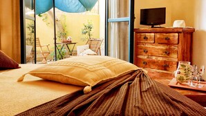 Une chambre d’hôtel avec un lit, une commode en bois, une télévision et une vue sur le balcon extérieur.