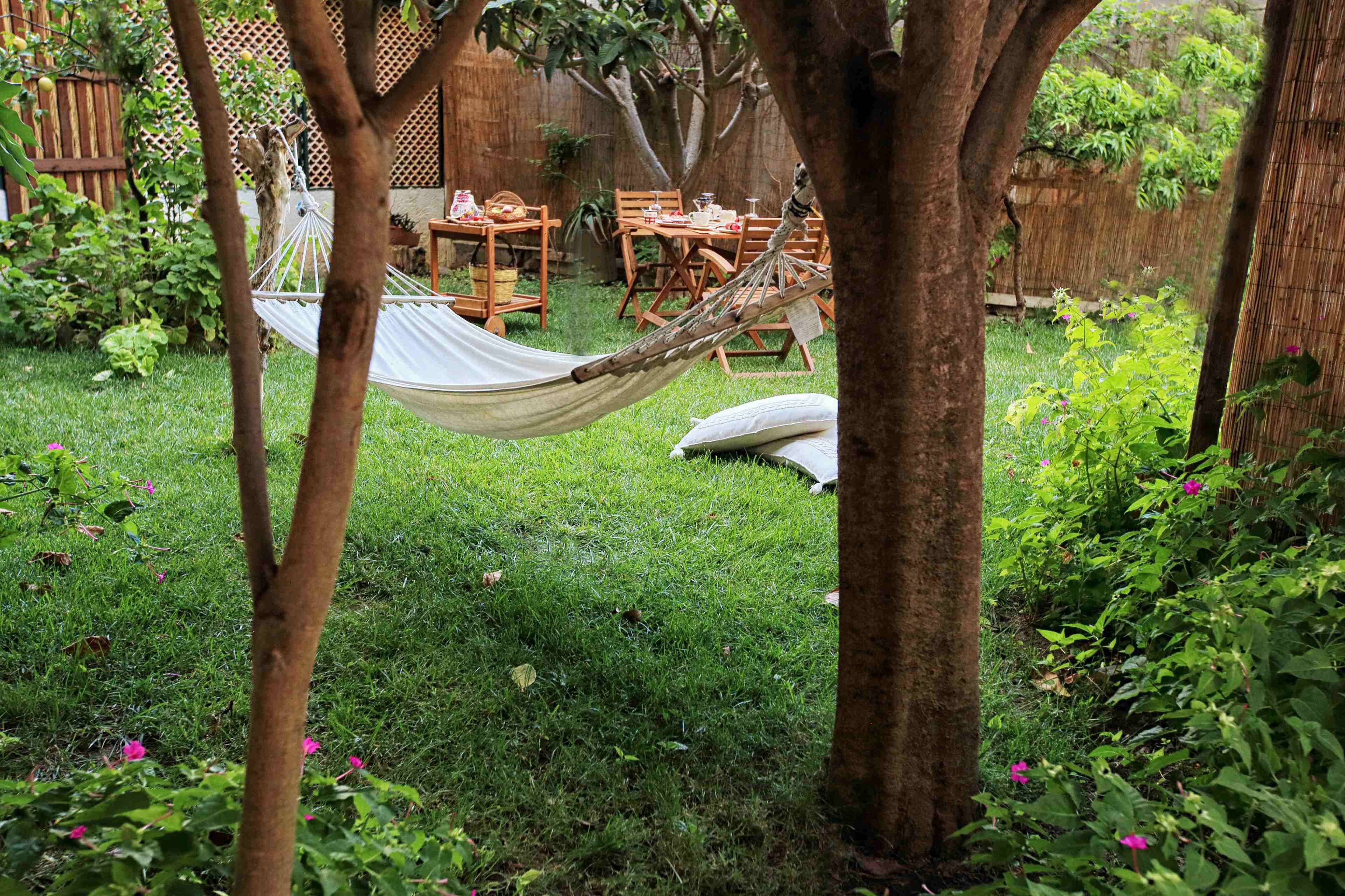 Eine Hängematze zwischen Bäumen in einem grünen Hinterhof mit einer Holzterrasse und Gartenmöbeln.