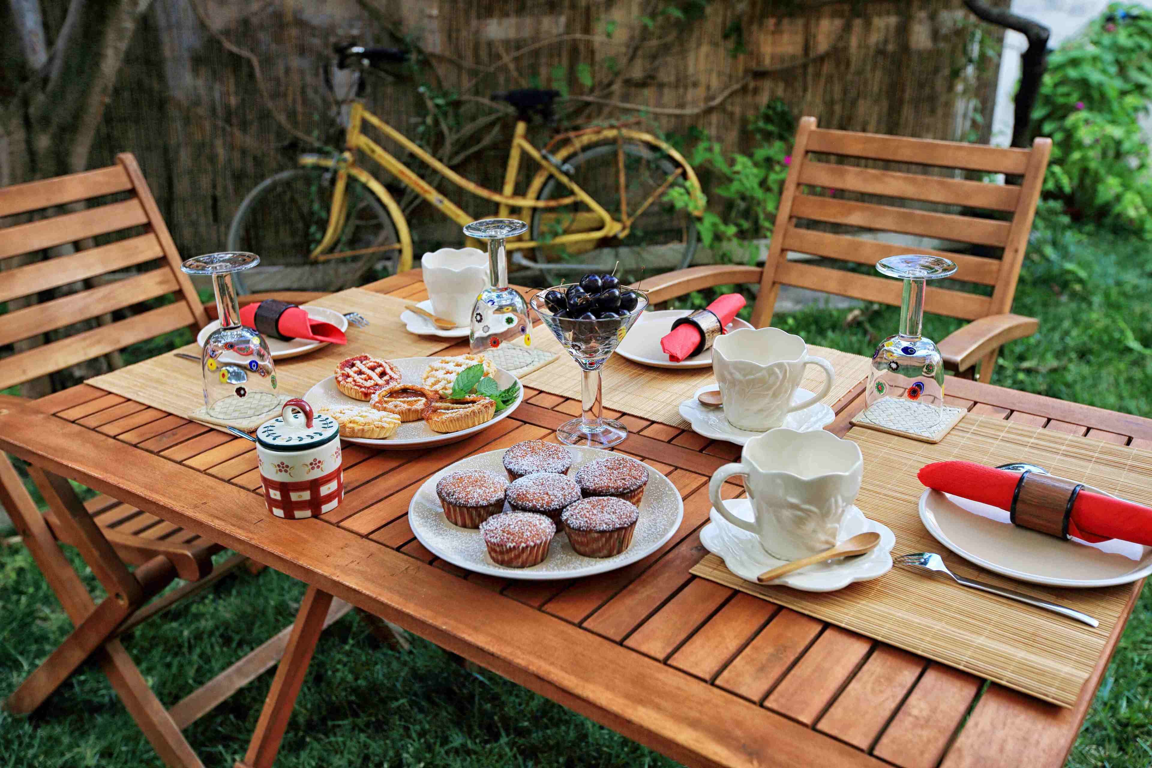 A wooden table set for a meal with plates of food, a glass of wine, and a bicycle in the background.