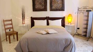 Quarto com cama, duas molduras na parede, abajur, cadeira de madeira e estante de metal.
