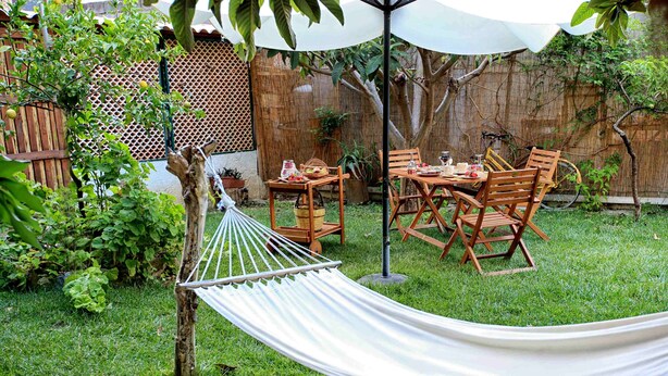 Eine Hängematte, Holzstühle, ein Tisch und ein Fahrrad in einem Garten mit Bambuszaun und viel Grün.