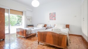 Une chambre à coucher avec deux lits en bois, une petite table, une chaise et une fenêtre avec des stores.