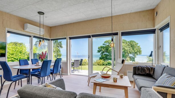 A spacious living area with a large window overlooking a scenic view, a dining area with blue chairs, and a cozy seating area with a sofa and a coffee table.
