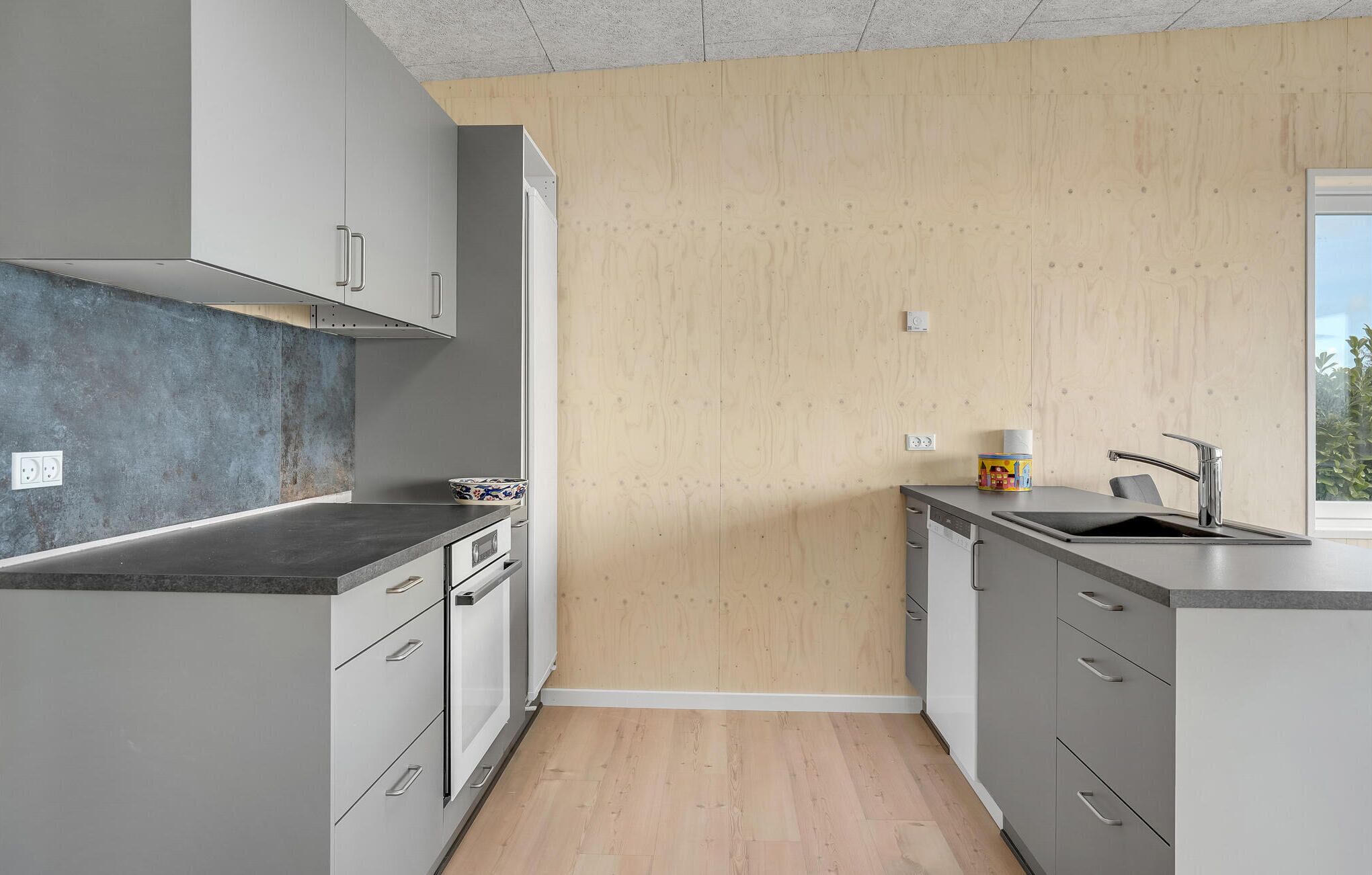 Une cuisine moderne avec des meubles gris, un plan de travail noir et un plancher en bois.