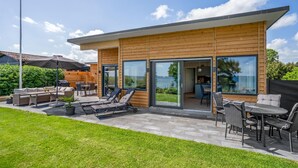 A modern house with a patio area featuring outdoor furniture, a dining table, and a large sliding glass door leading to an interior space.