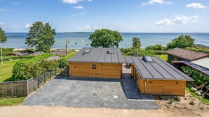 A wooden cabin with a gravel driveway and a view of the sea.