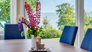 A dining table with a vase of flowers, two chairs, and a view of the sea through large windows.