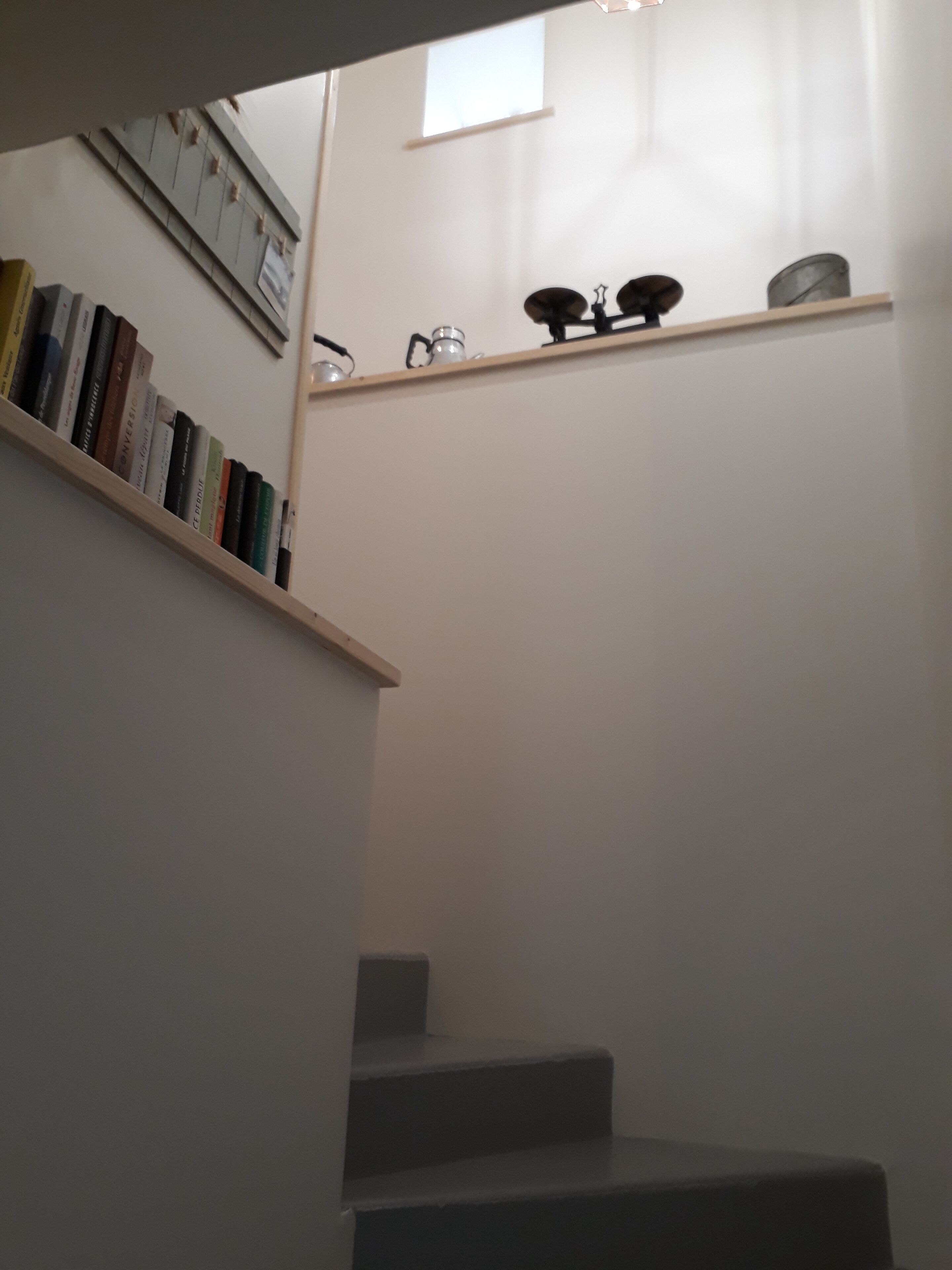 Una escalera con una estantería a la izquierda y una repisa con utensilios de cocina a la derecha.