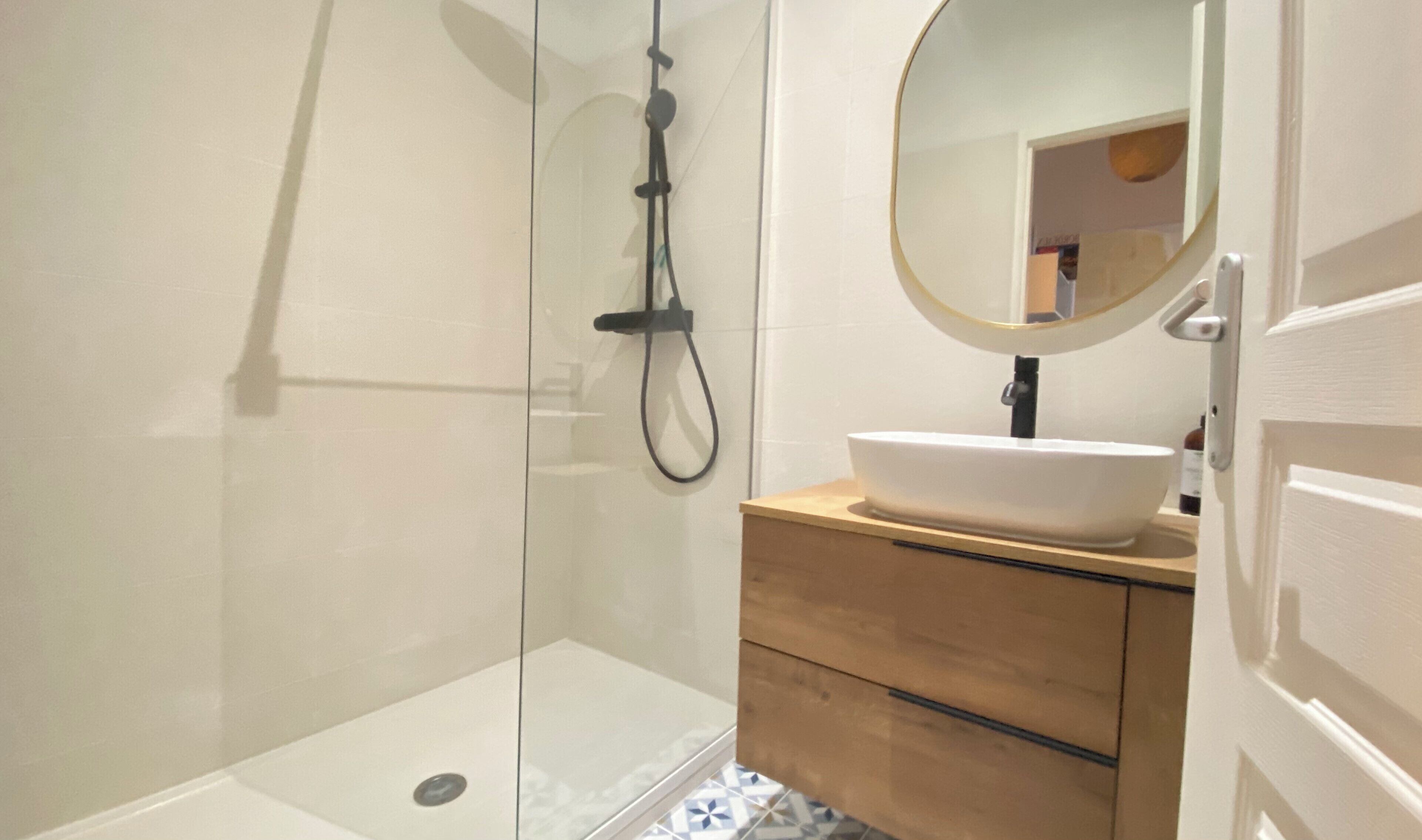 A modern bathroom with a glass shower enclosure, a white sink with a wooden vanity, and a round mirror.