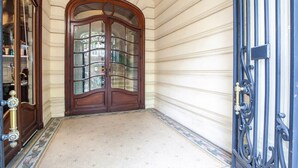 Une entrée imposante, avec une porte en bois et des panneaux de verre, qui donne sur un couloir au sol décoré de motifs.