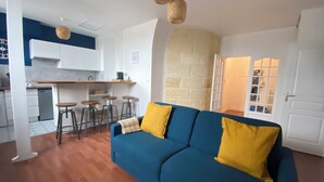 Un espace de vie compact comprenant un coin cuisine, un canapé bleu avec des coussins jaunes et un mur d’accent en pierre.